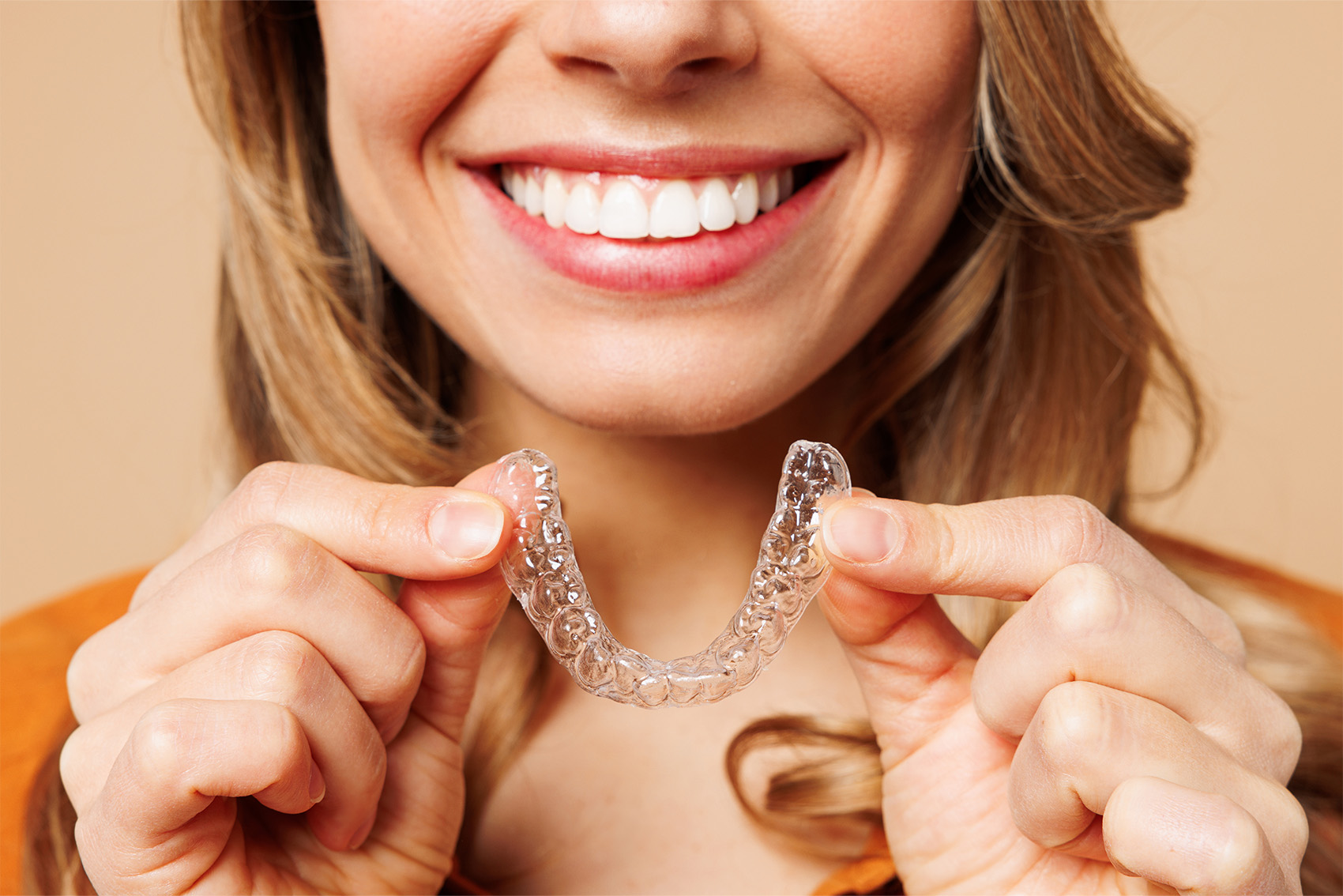 Woman smiling while holding clear aligners.